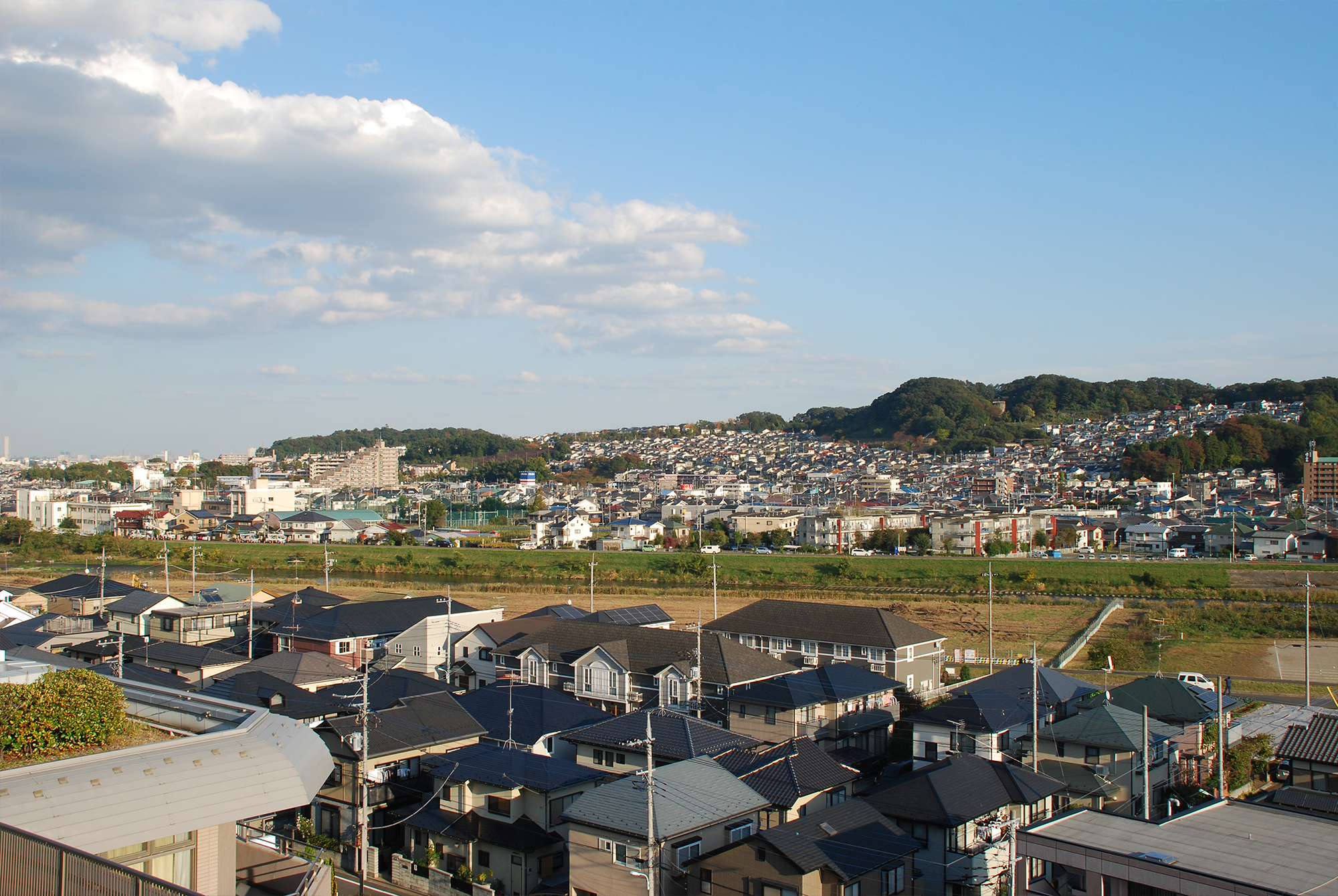 施設周辺の広い風景。川や田畑、遠景に山々と住宅地が見える。